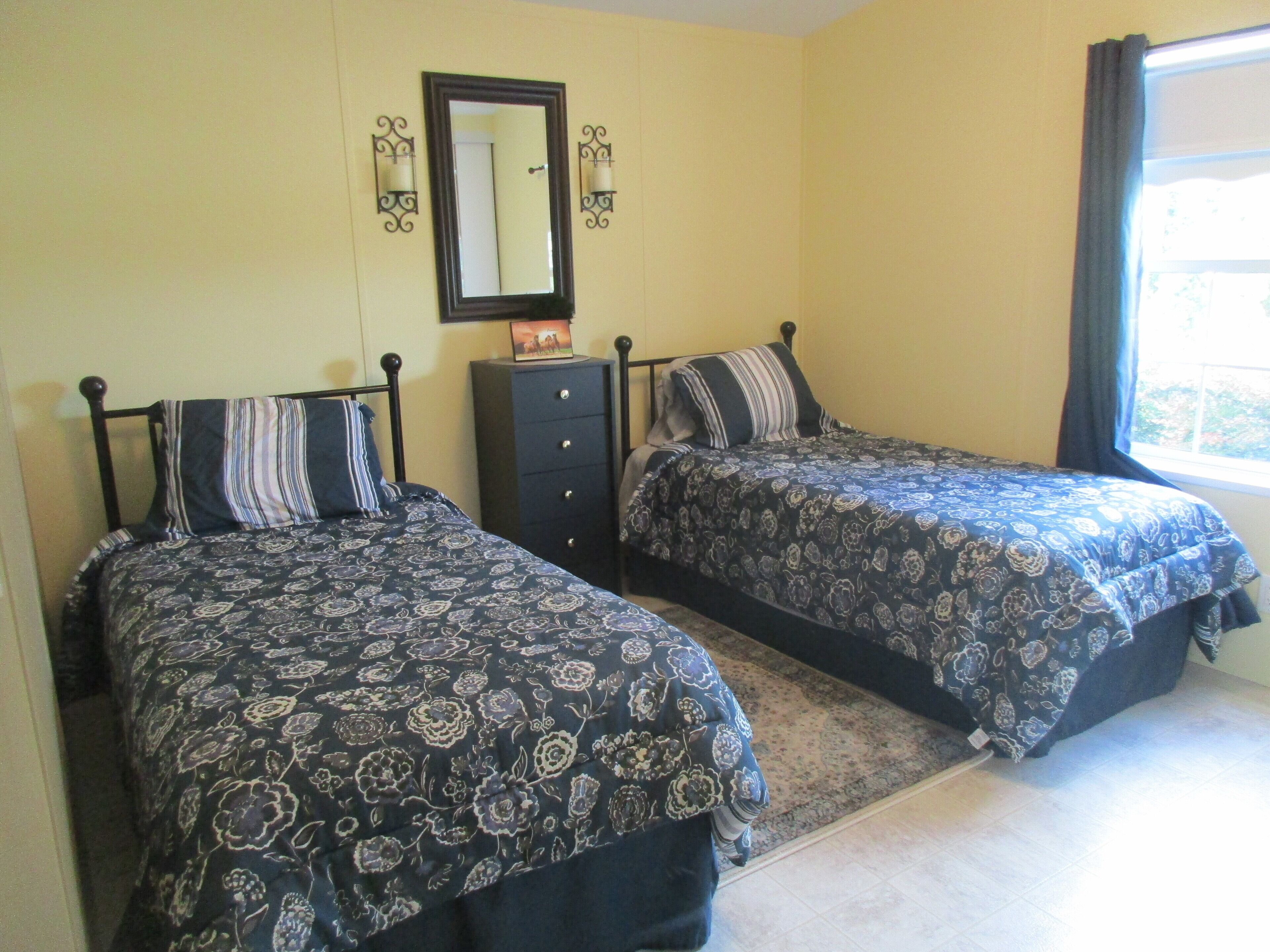 A bedroom with two beds, a dresser, a mirror, and a window with curtains.