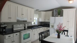 A kitchen with white cabinets, a stove, a microwave, and a refrigerator. There is a dining table with chairs and a vase of flowers.
