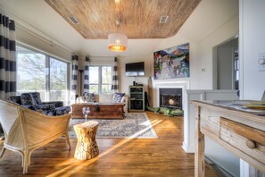 Un salon spacieux doté d’un plafond en bois, d’une cheminée et de grandes fenêtres.
