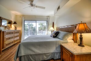 Ein Schlafzimmer mit Bett, Nachttisch, Deckenventilator, einem Holzschrank und Blick ins Freie.
