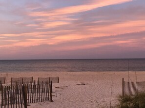 Ein Strand mit hölzernen Zäunen und einem ruhigen Meer unter einem rosafarbenen Himmel.