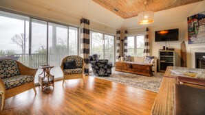 Amplia sala de estar con ventanas grandes, techo de madera y una lámpara moderna.