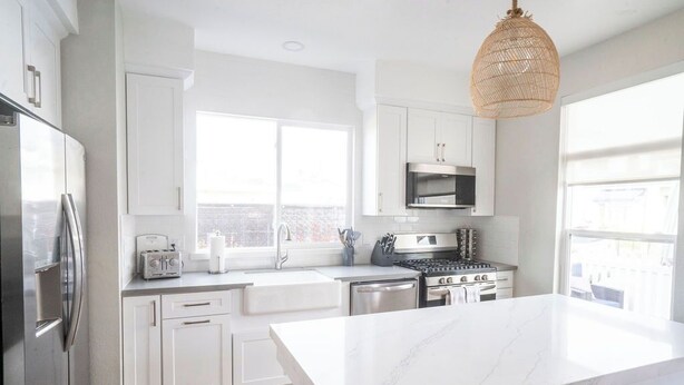 A modern kitchen with white cabinets, a marble countertop, stainless steel appliances, and a large window providing natural light. - Beautiful 6bd/7bath steps to the sand (Newport Beach)