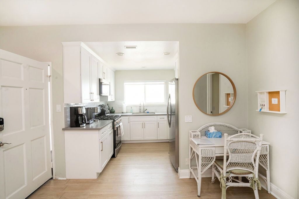 A modern kitchen with white cabinets, a coffee machine, and a dining area with wicker chairs.