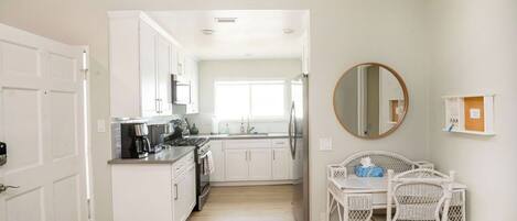 A modern kitchen with white cabinets, a coffee machine, and a dining area with wicker chairs.