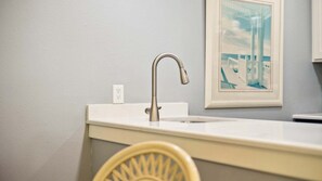 A bathroom with a white sink, a silver faucet, a framed picture on the wall, and a yellow chair.
