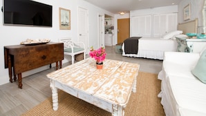A bedroom with a bed, a white sofa, a wooden coffee table with flowers, a TV, and a ceiling fan.