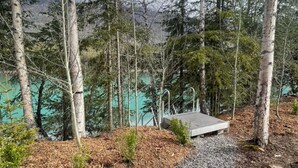 Eine Holzterrasse mit einer Bank, die auf einen Wald und ein türkisblaues Gewässer blickt.