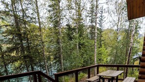 Eine Holzterrasse mit Picknicktischen und -stühlen, umgeben von Bäumen und mit Blick auf ein Gewässer.