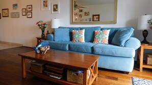 Una sala de estar con un sofá azul, una mesa de centro de madera y un espejo grande en la pared.