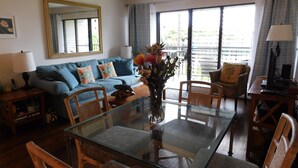 Una sala de estar con una mesa de centro de vidrio, sofá azul y un ventanal con cortinas.