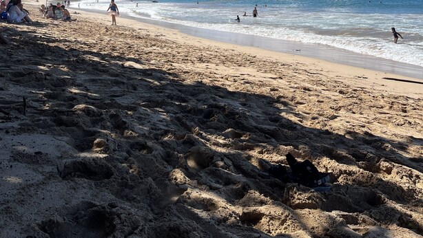 Una playa con cielos despejados, gente nadando y caminando, y una montaña distante.