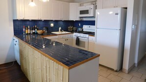 Una cocina moderna con armarios blancos, un salpicadero de azulejos azules, una isla central y electrodomésticos blancos que incluyen una estufa, un microondas y un refrigerador.