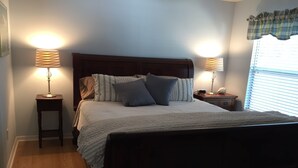 A neatly made bed with a wooden headboard, flanked by two bedside tables with lamps, in a room with wooden flooring. - Charming 3/2 Virginia Trace Villa, next to Lake Sumter Landing, with golf cart (The Villages)