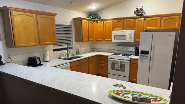 A kitchen with wooden cabinets, a microwave, a stove, a sink, and a refrigerator. - Charming 3/2 Virginia Trace Villa, next to Lake Sumter Landing, with golf cart (The Villages)