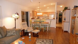A cozy living room with a sofa, armchair, and coffee table. A dining area with chairs and a table is visible in the background. - Charming 3/2 Virginia Trace Villa, next to Lake Sumter Landing, with golf cart (The Villages)