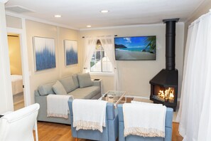 A living room with a sofa, armchairs, a glass coffee table, a fireplace, and a painting of a beach scene.