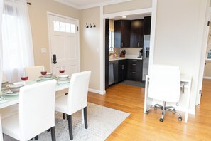 A dining area with a table set for four, a white office chair, and a kitchen visible through an open door.