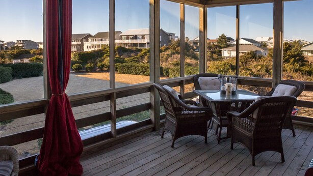 Eine überdachte Terrasse im Freien mit Korbmöbeln und einem Tisch, mit Blick auf eine Wohngegend mit Häusern und Grünflächen.