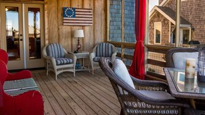 Eine Holzterrasse mit Korbmöbeln, einer Flagge und Blick auf ein Haus.
