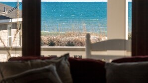 Blick aus einem Fenster auf einen Strand mit Meer und einem Gebäude im Hintergrund.
