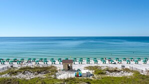 A beach with rows of green umbrellas and beach chairs, a lifeguard tower, and a sandy area with sparse vegetation. - Beachfront Condo!Beautiful View, On the Beach! Unit 308 (Destin)