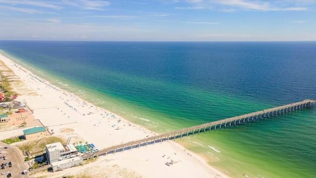 Une plage avec une longue jetée qui s’avance dans l’océan, une plage de sable et quelques bâtiments le long du rivage.