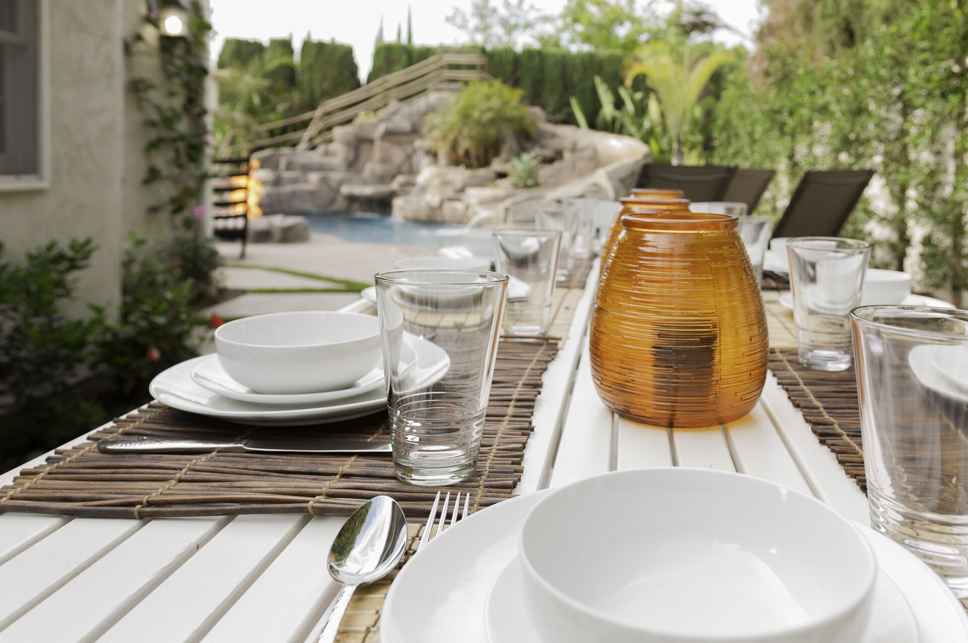 A dining table set outdoors with white plates, bowls, glasses, and a decorative vase.
