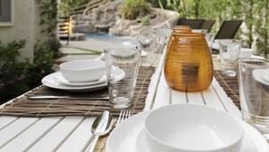 A dining table set outdoors with white plates, bowls, glasses, and a decorative vase.