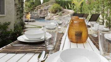 A dining table set outdoors with white plates, bowls, glasses, and a decorative vase.