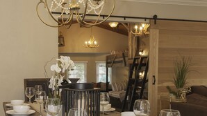 A long dining table set with white plates, bowls, and wine glasses, a chandelier above, and a wooden accent wall.