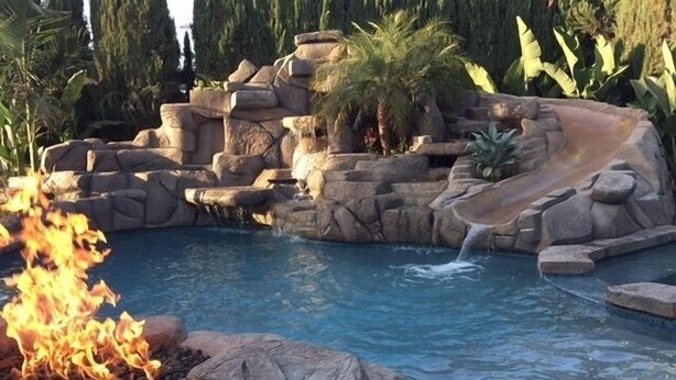 A pool with a rocky landscape, a waterfall feature, and a fire pit.