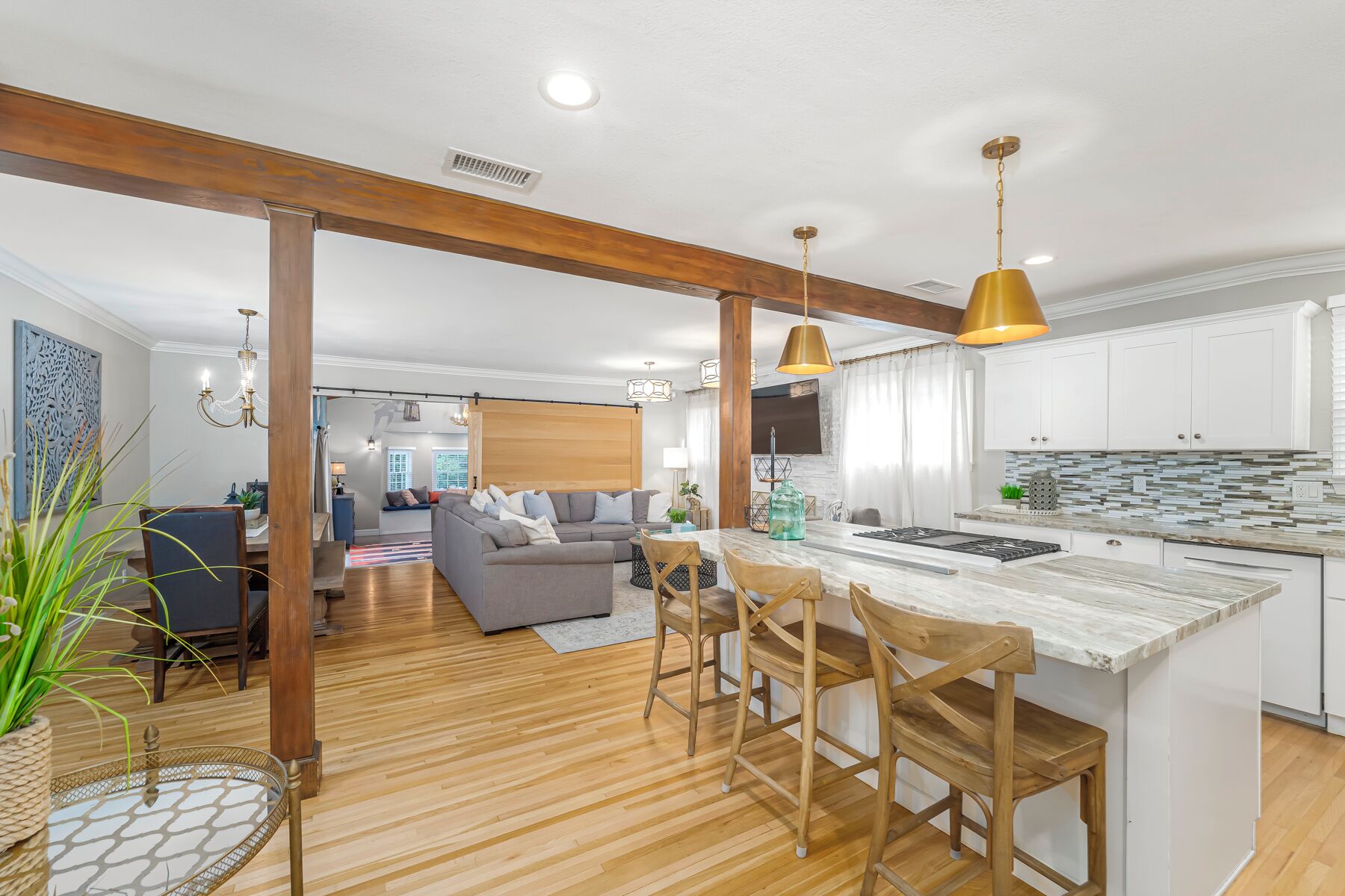 A modern kitchen with wooden beams, a marble island, and a dining area with a sofa and chairs.