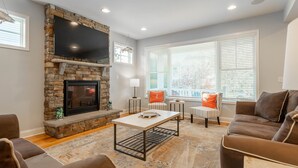 A living room with a stone fireplace, a flat-screen TV, and a large window with blinds. - Spacious Rehoboth/Dewey Beach House Sleeps 17 (Rehoboth Beach)