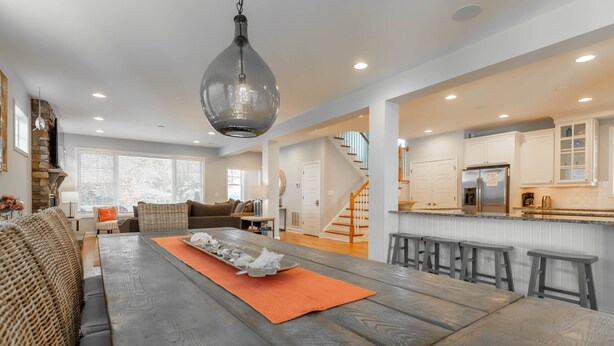 A spacious living area with a large wooden dining table, a sofa, and a kitchen area with white cabinets and a stainless steel refrigerator. - Spacious Rehoboth/Dewey Beach House Sleeps 17 (Rehoboth Beach)