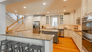 A spacious kitchen with white cabinetry, a granite island with bar stools, a stainless steel refrigerator, and a microwave. - Spacious Rehoboth/Dewey Beach House Sleeps 17 (Rehoboth Beach)