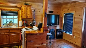 L’intérieur d’une cabane est doté de murs en bois, d’un coin cuisine avec une cuisinière, un évier et un comptoir, d’une cheminée et d’un téléviseur fixé au mur.
