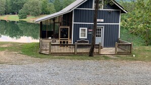 Une petite cabane bleu foncé, dotée d’un porche et d’une enseigne indiquant qu’il s’agit d’un lieu de pêche, située près d’un lac, avec une forêt en arrière-plan.