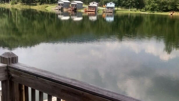 Une terrasse en bois surplombe un lac paisible, avec plusieurs cabanes visibles au loin.