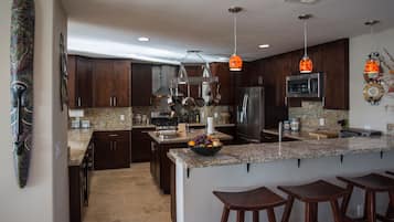 A modern kitchen with granite countertops, stainless steel appliances, and wooden bar stools.