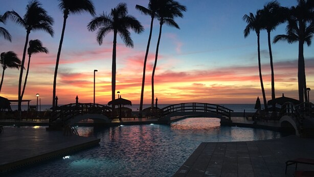 A sunset view over a pool area with palm trees and a bridge. - Ground Floor, Oceanview And Oceanfront  (San Jose del Cabo)