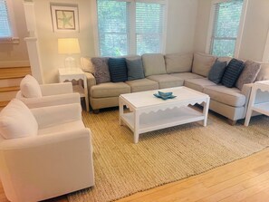 A living room with a beige sofa, white armchairs, a white coffee table, and a rug.