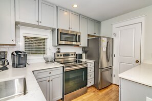 A modern kitchen with stainless steel appliances, white cabinetry, and a wooden floor. - 3BR/3.5 BA home with private crofter. Nature views and access to Shoals Club! (Bald Head Island)