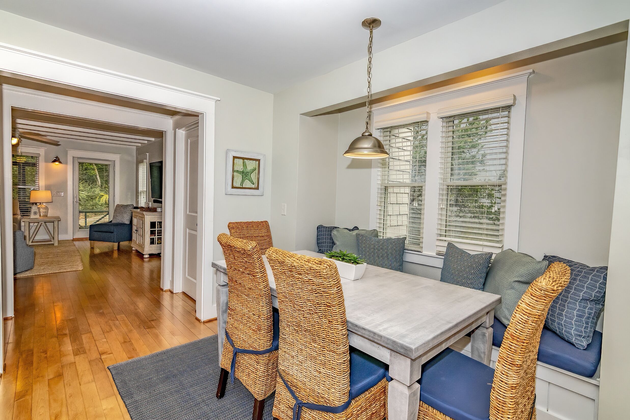 A dining area with wicker chairs, a wooden table, and a hanging light fixture.
