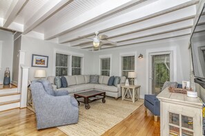 A living room with a sectional sofa, a blue armchair, a coffee table, and a ceiling fan. - 3BR/3.5 BA home with private crofter. Nature views and access to Shoals Club! (Bald Head Island)
