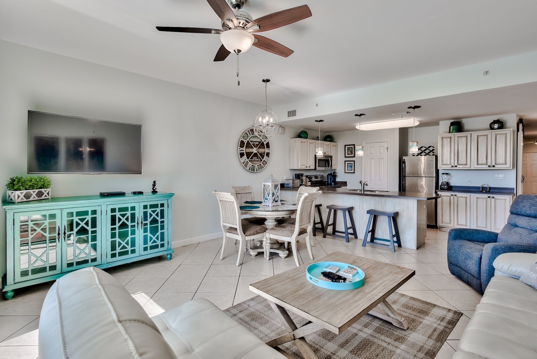 A modern living room with a dining area, kitchen, and a TV mounted on the wall.