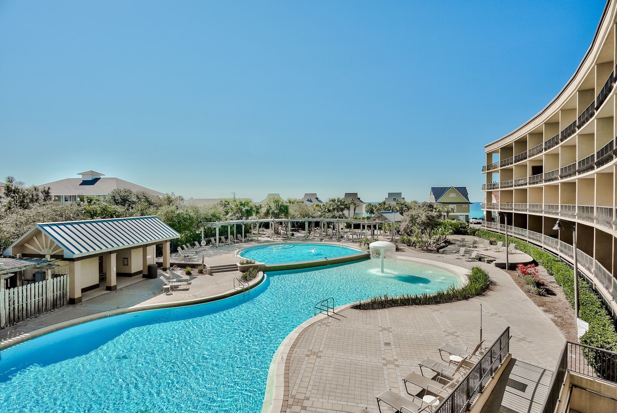 A resort with a large pool area, including a circular pool and a separate pool, surrounded by lounge chairs and a covered seating area.