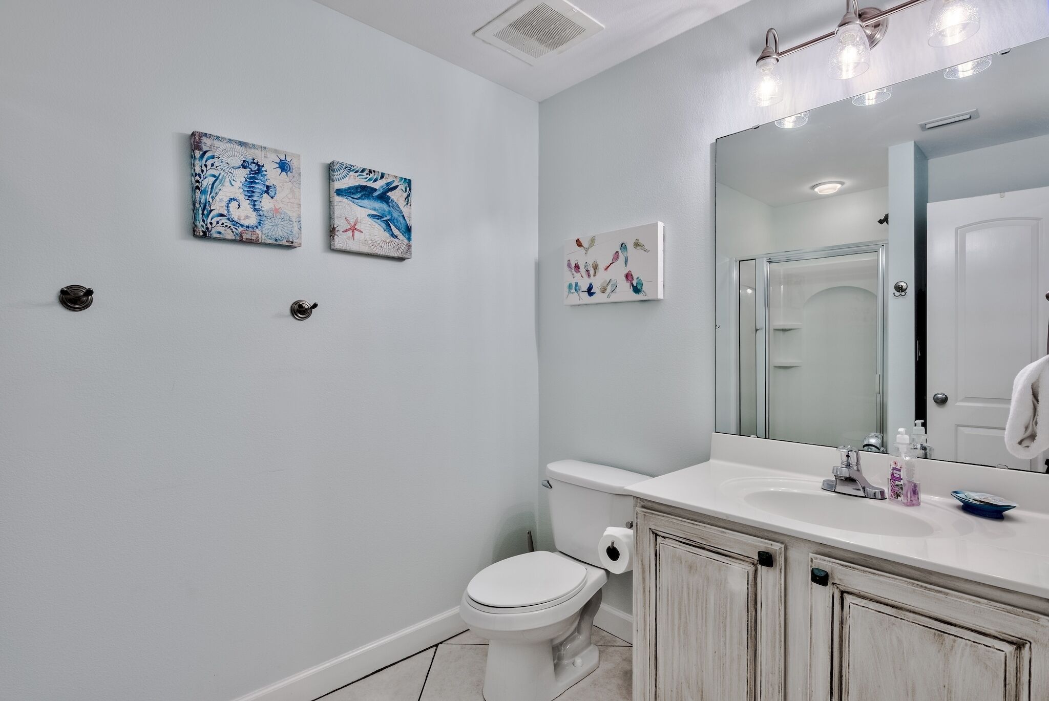 A bathroom with a white toilet, a sink with a mirror, and two wall-mounted artworks.
