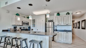 A modern kitchen with white cabinets, a central island with bar stools, stainless steel appliances, and pendant lighting. - Relax and Enjoy Gulf Views & Excellent Pools, 3rd floor, Garage Parking (Miramar Beach)