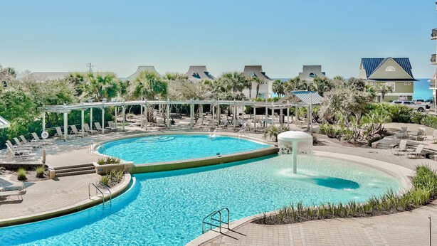A swimming pool with lounge chairs and a covered area, surrounded by greenery and buildings. - Relax and Enjoy Gulf Views & Excellent Pools, 3rd floor, Garage Parking (Miramar Beach)